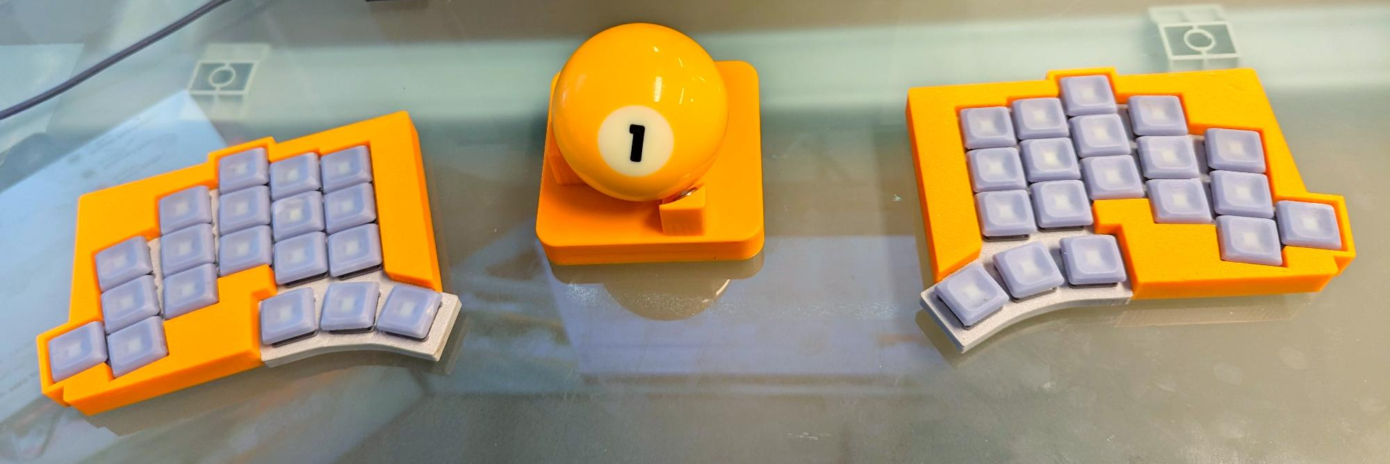 A Totem split keyboard in yellow, with a #1 pool ball trackball in between the halves.