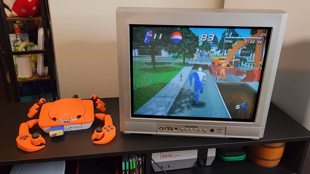 An orange PSOne in the shape of a crab sits next to a large CRT monitor displaying a video game of a person running through what appears to be a park. A Pepsi logo is toward the top of the HUD.