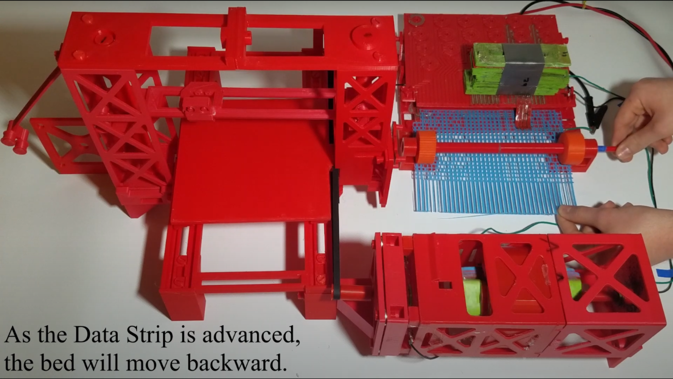 A 3D printer frame made of red plastic is shown on the left-hand side of the image. On the right-hand side, there is a large motor with a plastic frame attached to the frame. Next to the 3D printer, a blue plastic mesh is being fed through a red plastic frame.