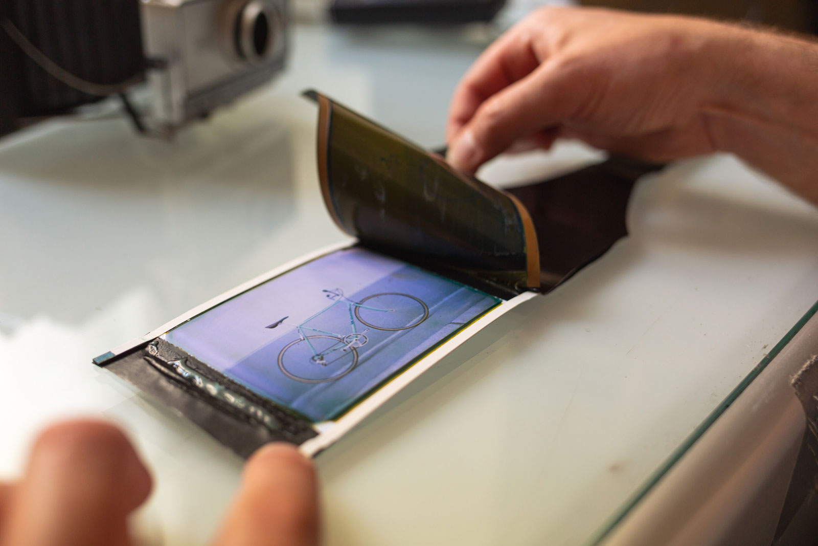 An instant photograph of a bicycle is being revealed, as the negative is peeled away from the print.
