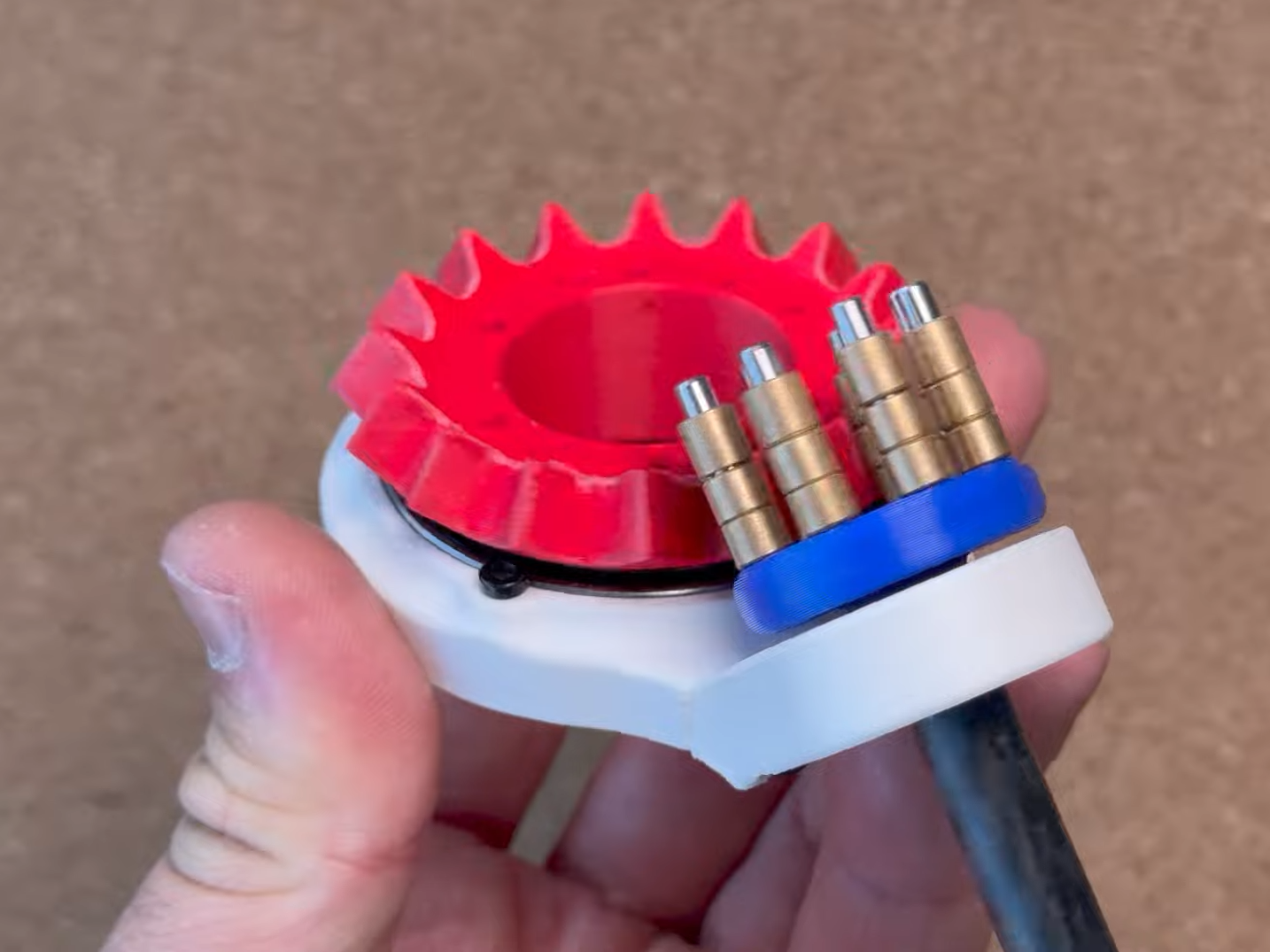 red crown gear on a white frame. Blue gear with brass rollers are engaged with the crown.