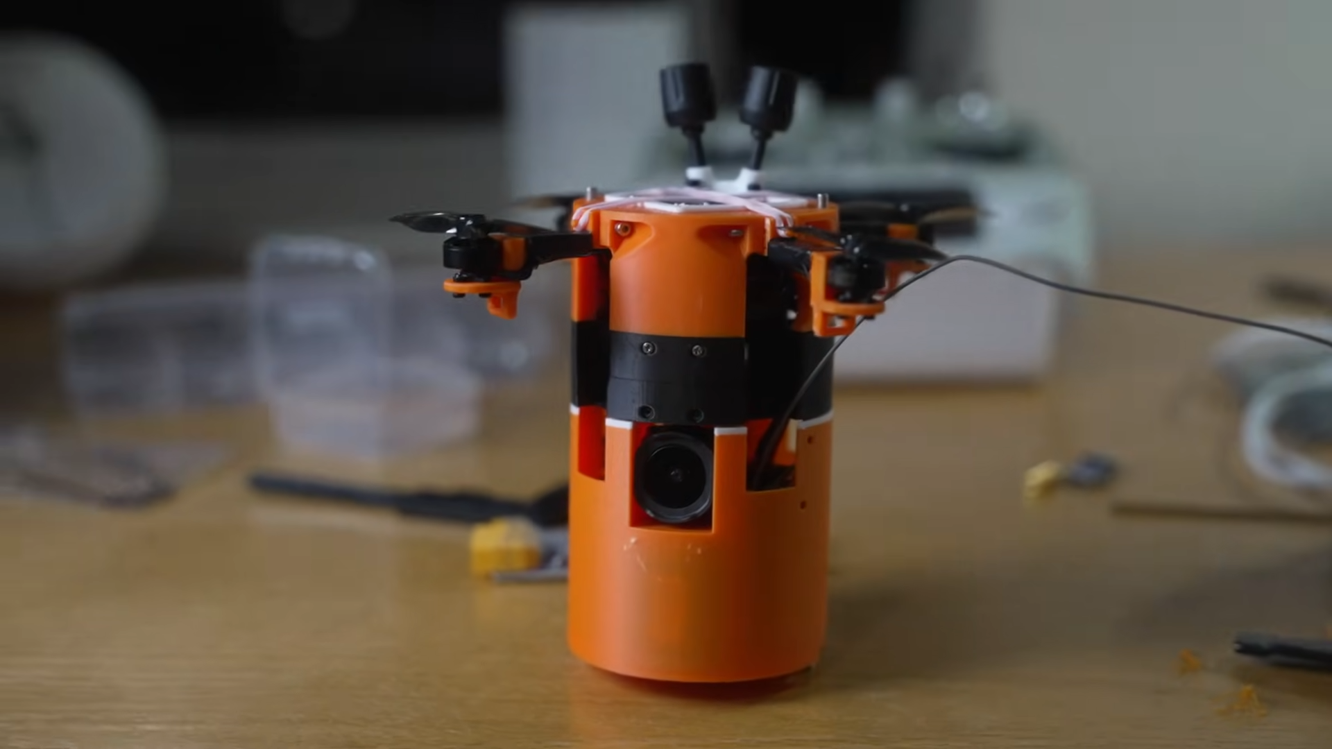 Picture of self landing drone satellite with orange and black body. Propellors are extended.