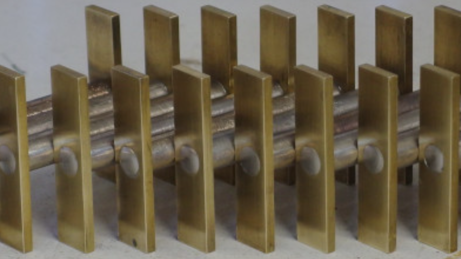There are a number of metal cylinders displayed in a line. Each cylinder has a rectangular brass plate mounted to each end, and these brass plates stand upright, with the metal cylinders held horizontally between them.