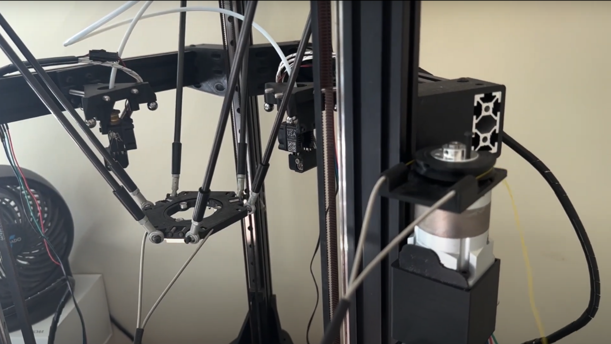 The frame of a delta 3D printer is shown. The toolhead of the 3D printer does not have a hotend installed, but instead has a frame with a circular hole in the middle.