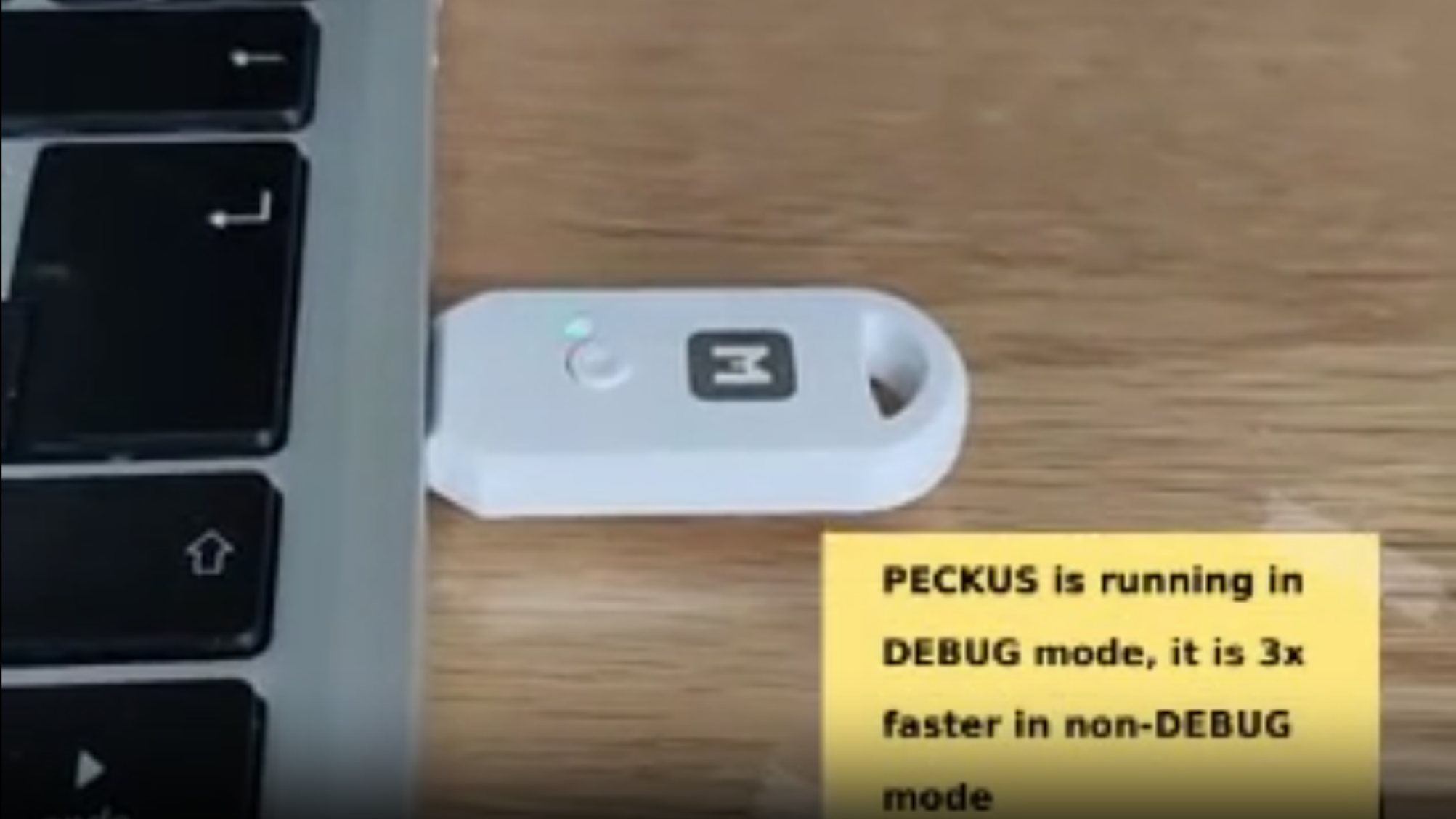 A USB dongle is shown connected to a laptop computer. A text box in the lower right corner says "PECKUS is running in DEBUG mode, it is 3x faster in non-DEBUG mode."