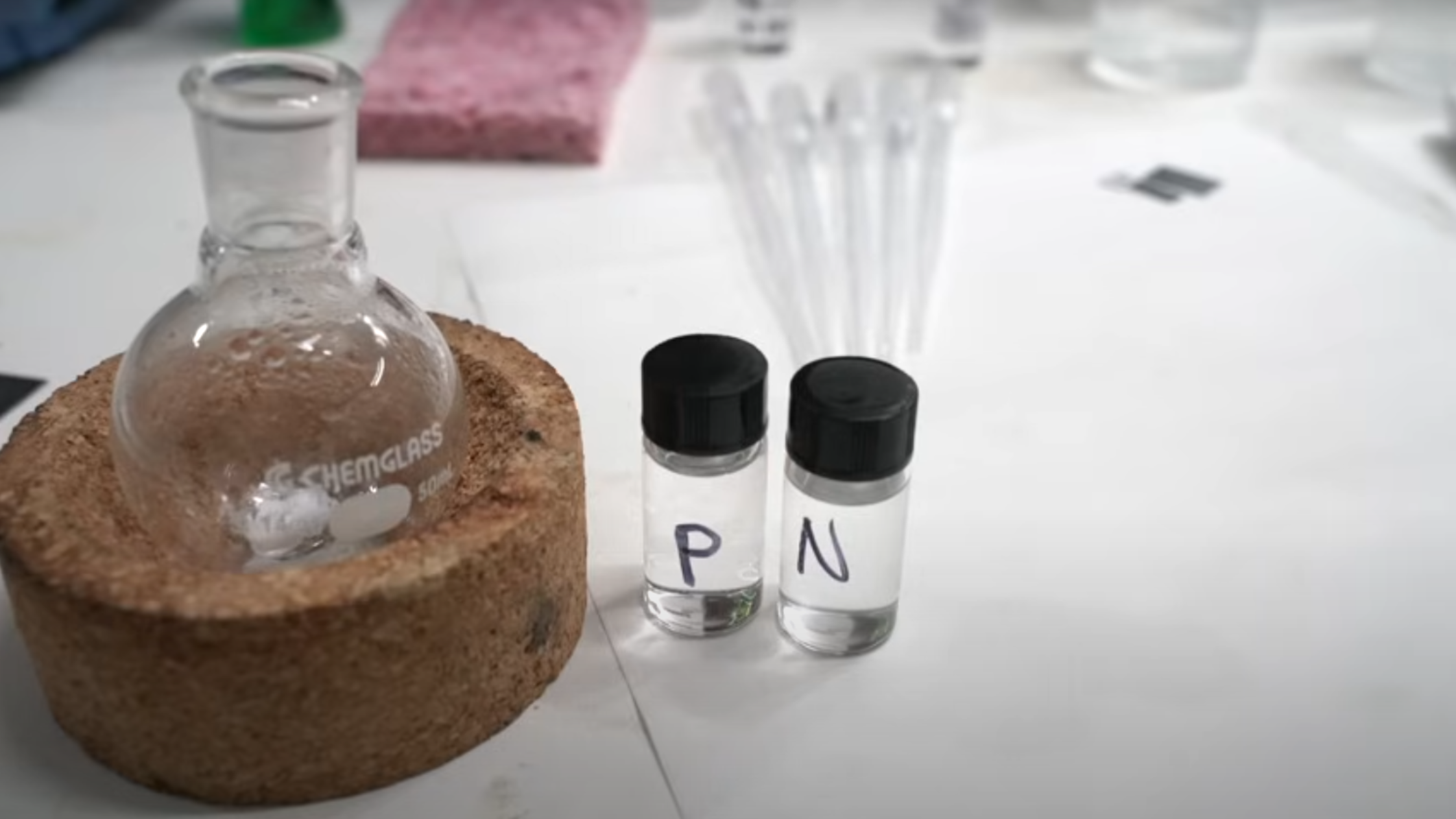 Two clear phials are shown in the foreground, next to a glass flask. One phial is labelled “P,” and the other is labelled “N”.