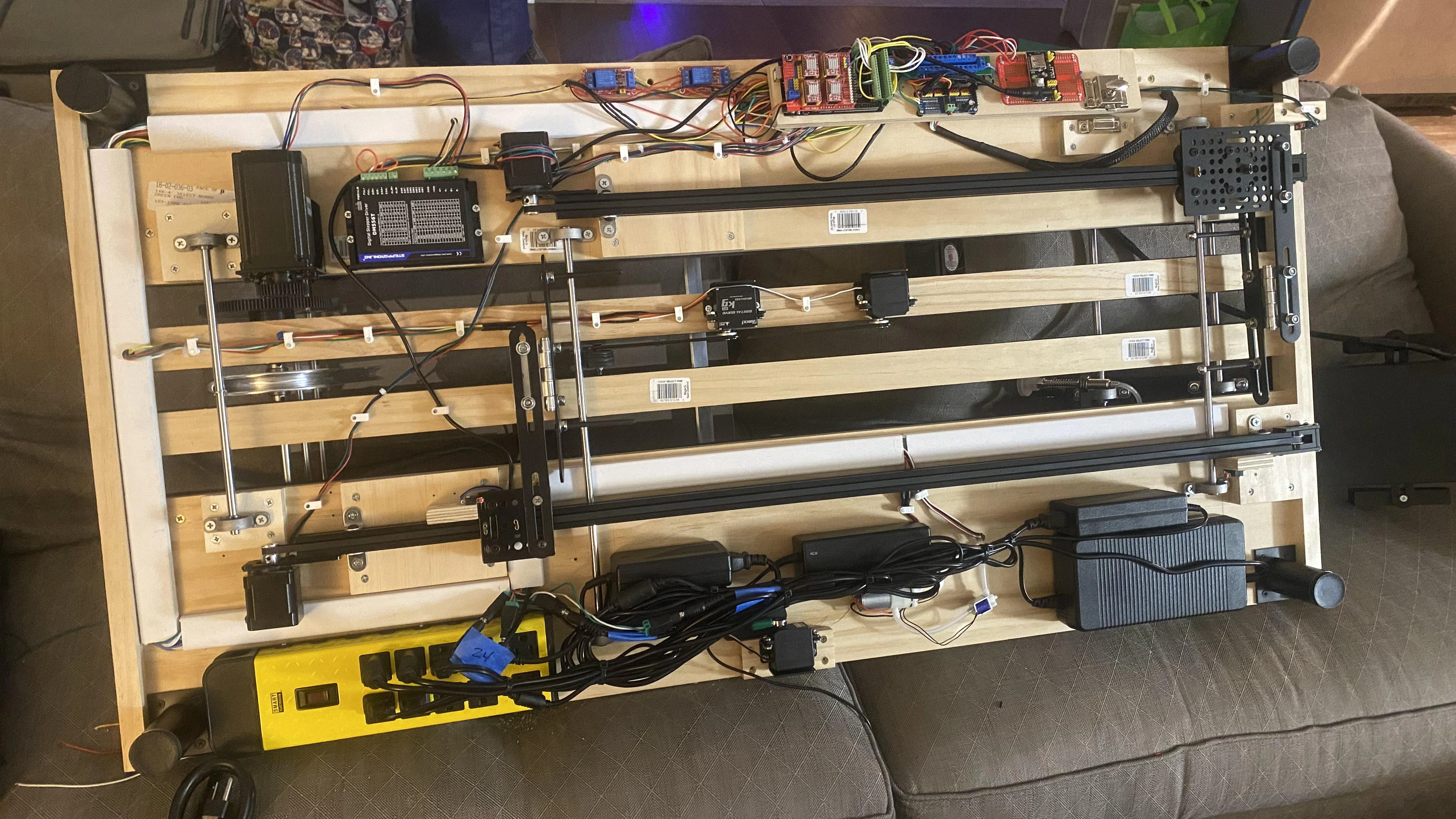 The underside of the scanner is shown. Four power supply units are visible on the lower side, and assorted electronics are visible on the top side. In the middle, two linear tracks adapted from a 3D printer run along the length of the scanner, and several motors can be seen mounted between the rails.