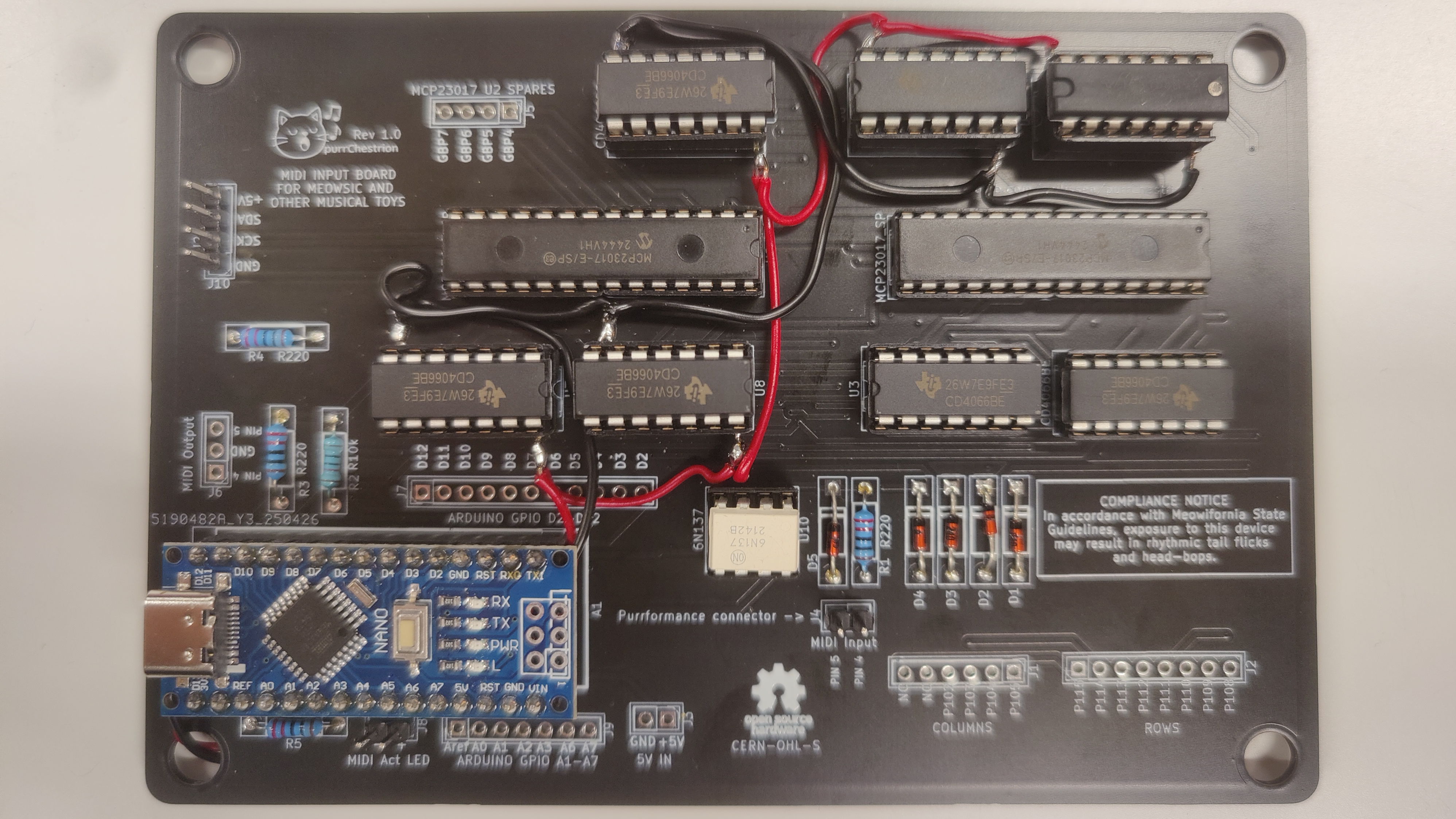 A black PCB is shown, with an Arduino Nano mounted in the bottom left corner. The rest of the space on the PCB is used up by ten DIP integrated circuits and a few resistors and diodes. Several black and red wires connect different parts of the PCB.