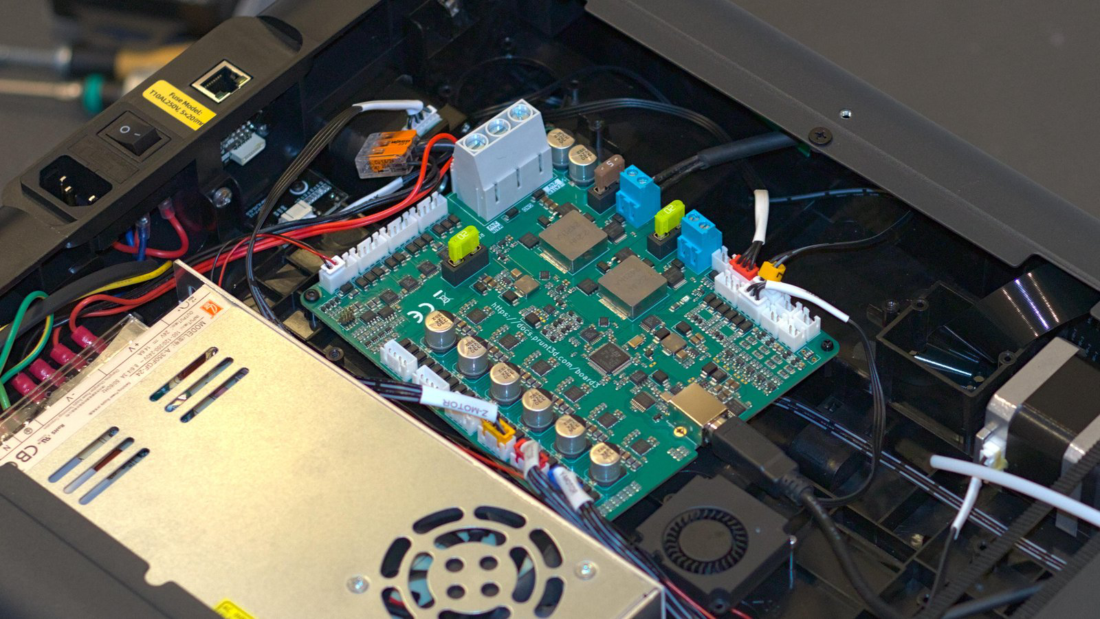 A Prunt 3D printer control board is shown mounted in a 3D printer, just behind a power supply, in the center of the image.