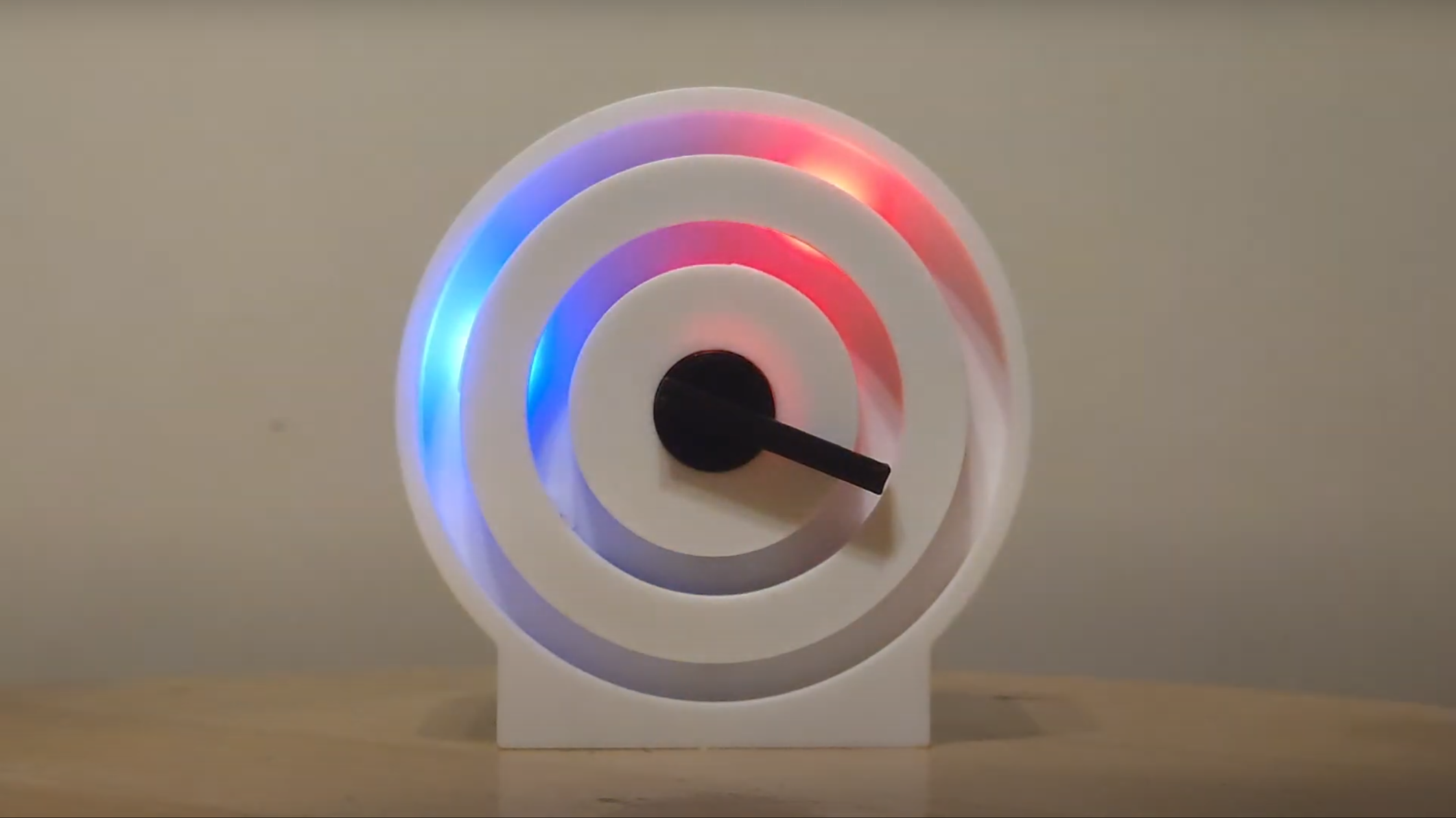 A clock face is shown consisting of two rings of plastic, with backlighting behind one of the rings. There is red light at the one o’clock position, and blue light at the nine-thirty position. A black plastic arm is pointing to the three-thirty position.