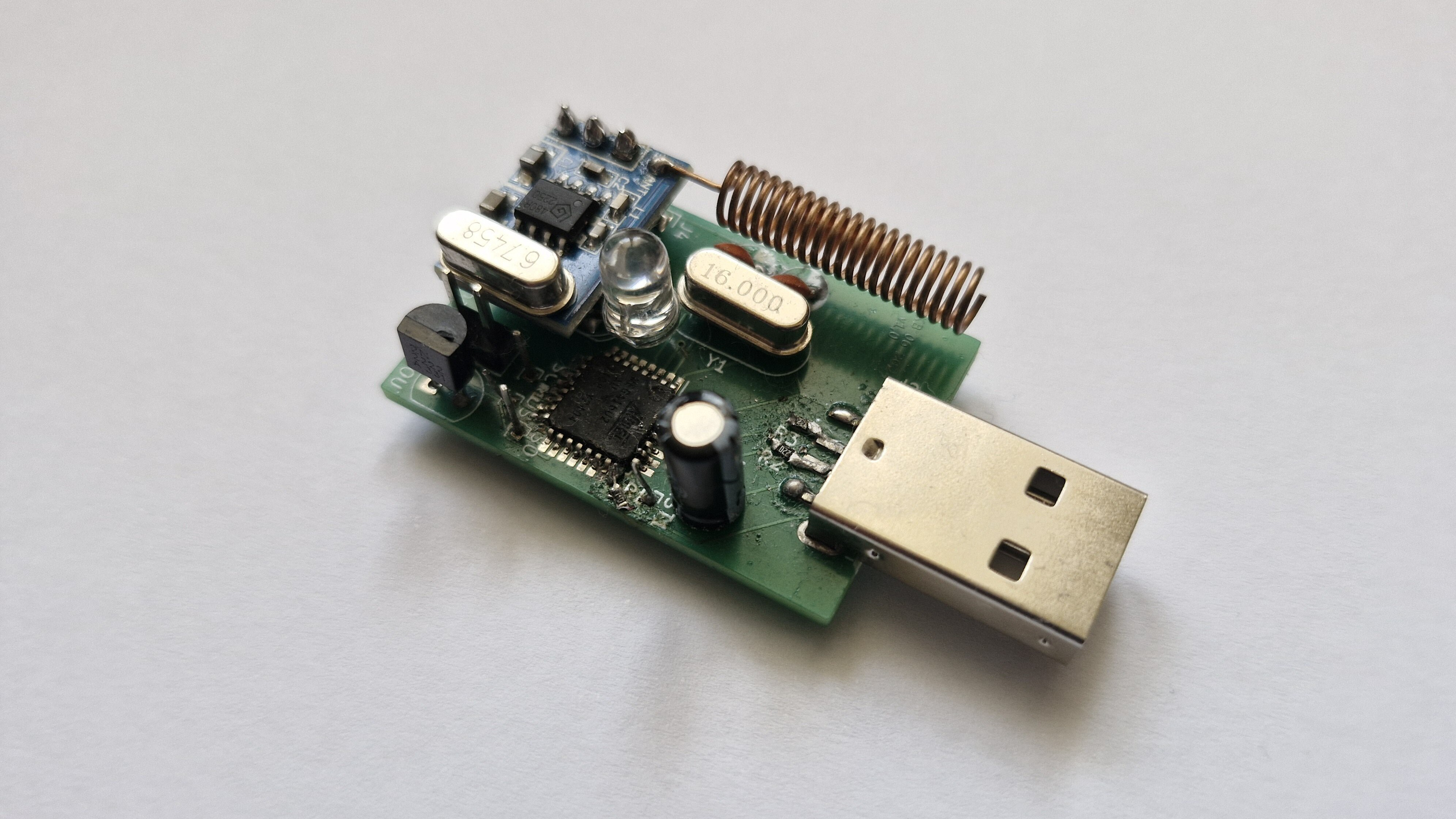A circuit board is shown on a white background. It has a USB-A port on the front side, and a coiled wire antenna extending from another circuit board mounted above the first one.