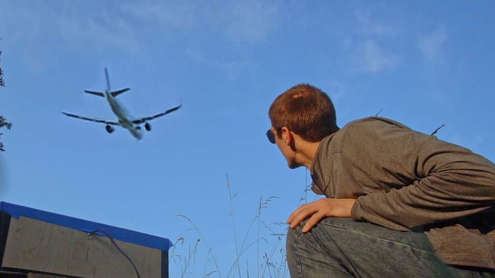 Photo of AlphaPhoenix looking at an airplane flying through the air