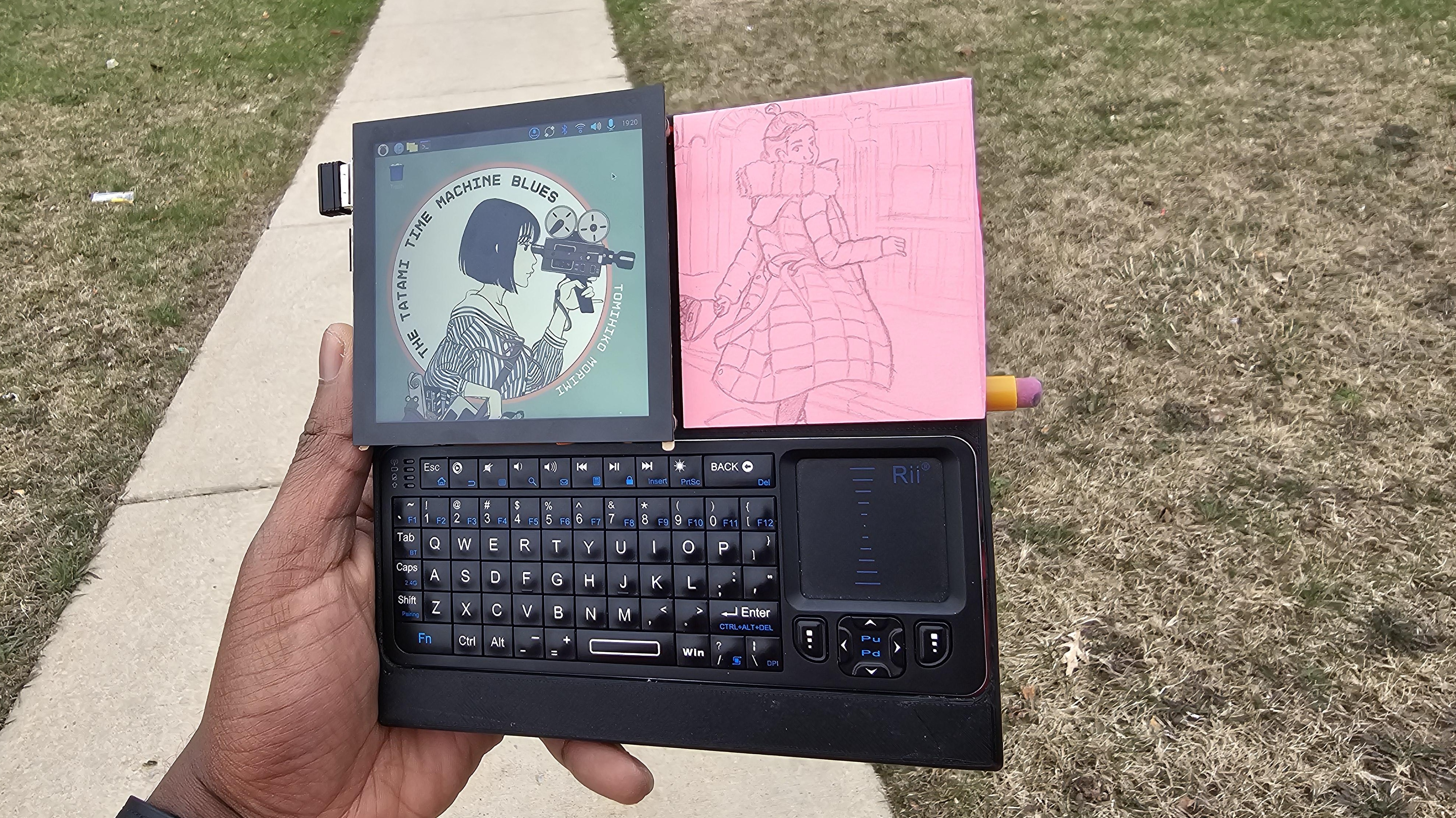 A hand with dark skin holds a black device. The bottom is a small keyboard and touchpad. The upper half is split with a square LCD on the left and a square, pink notepad on the right. A sketch of a woman wearing a puffy jacket is on the notepad and an illustration of a woman looking through an old timey film video camera is on the screen on the left.
