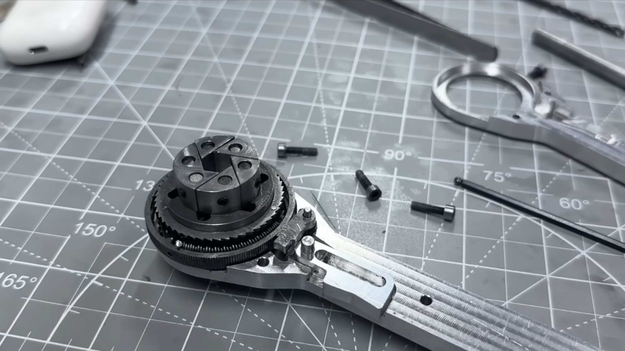 A wrench is shown lying on a machinist’s mat. The end of the wrench holds a ratcheting wheel, on top of which are six independent metal blocks arranged into a hexagon.