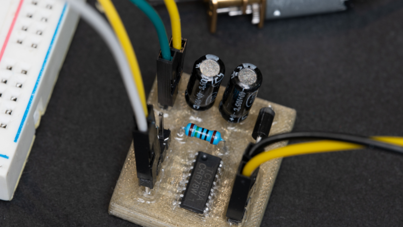 A brown plastic circuit board is visible in the middle of the picture, containing an integrated circuit, a resistor, a diode, two capacitors, and some jumper wires going away to the sides.