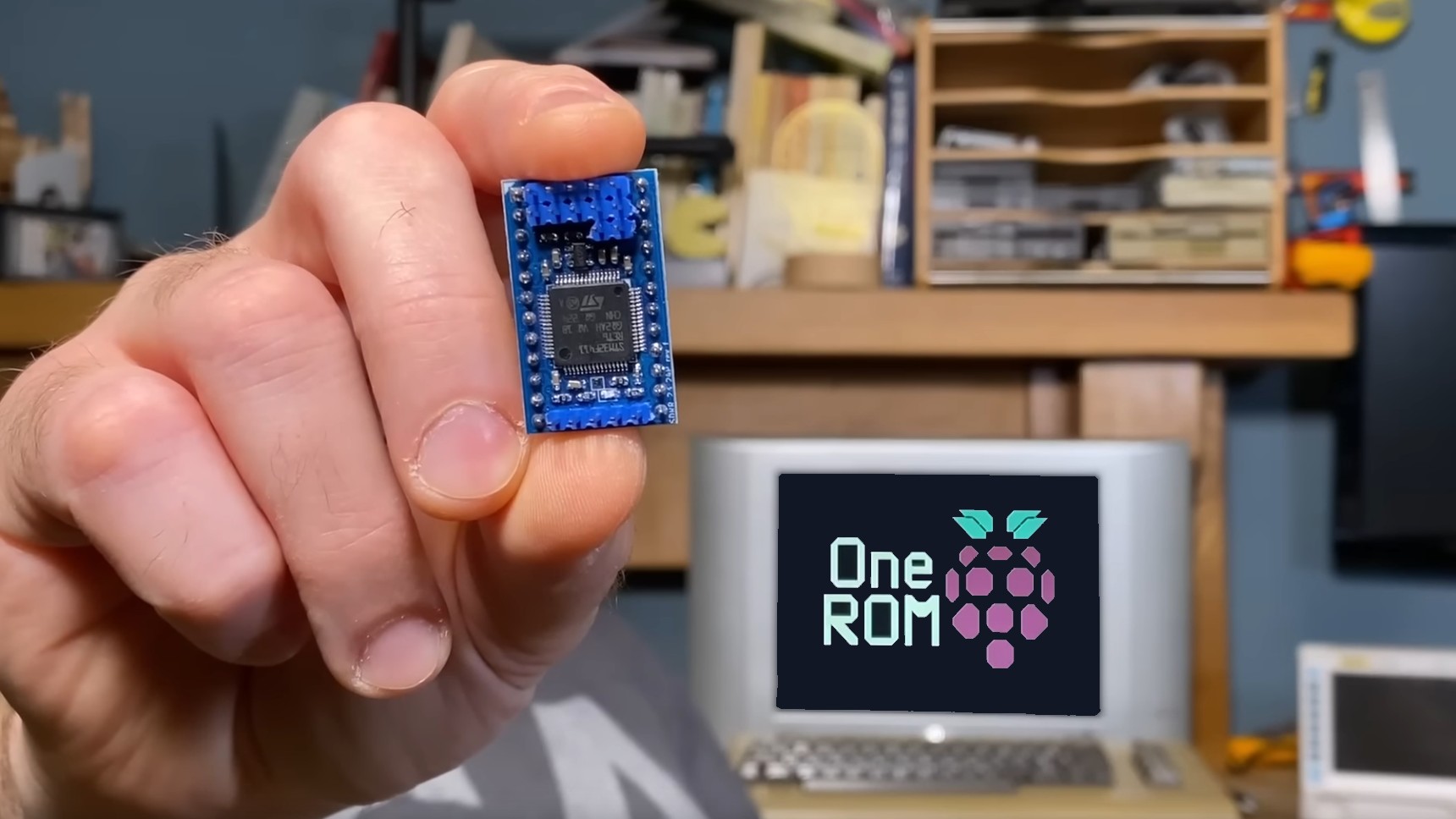 A hand holding a One ROM with a Commodore 64 in the background