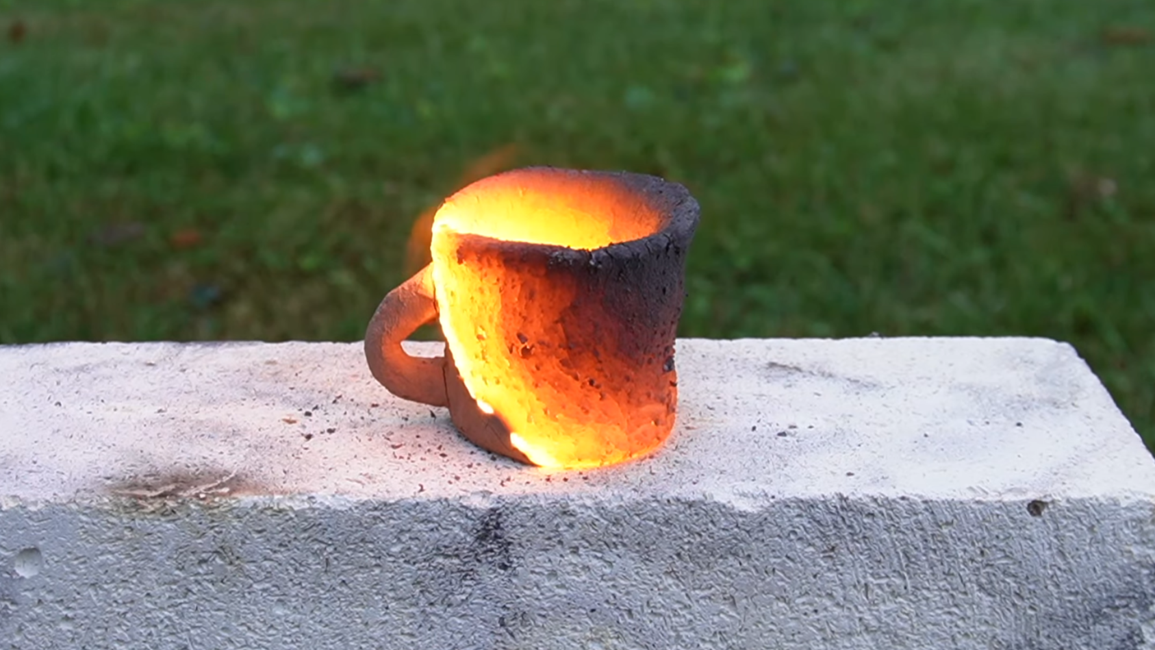 A clay mug is placed on a fire brick. Portions of the mug are glowing orange hot, and the heat is spreading across the surface. Some portions of the mug have cooled, and the heat has not reached other parts.