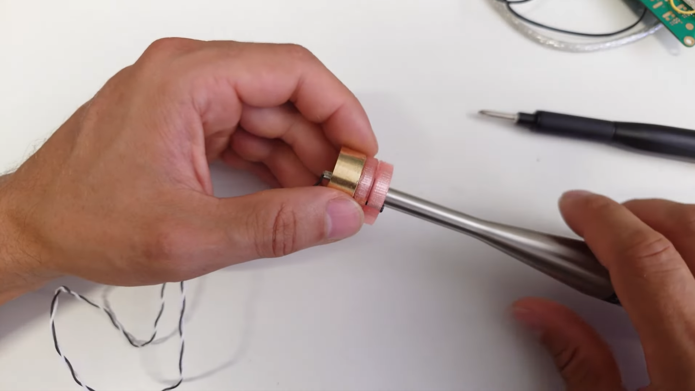 A man's hands are shown holding a microphone capsule with a 3D-printed part on top of it, with a flared metal tube protruding from the plastic.