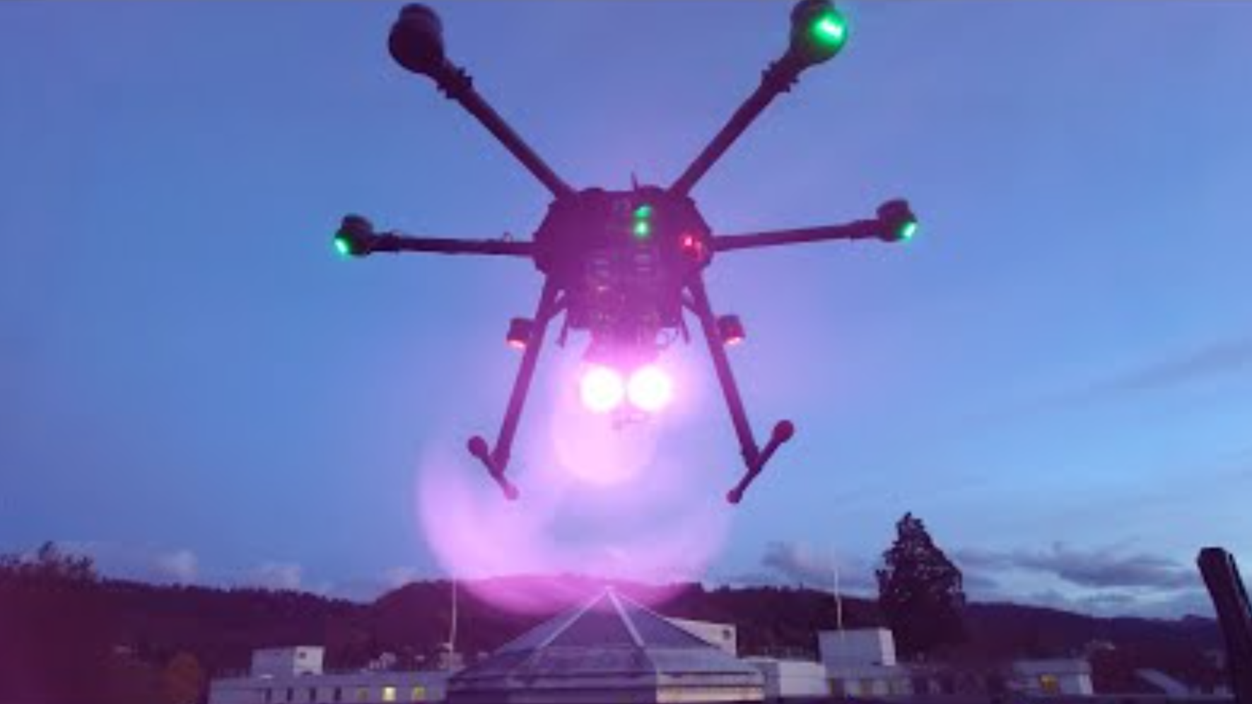 A drone is shown hovering in the sky, with two bright lights shining from its underside.