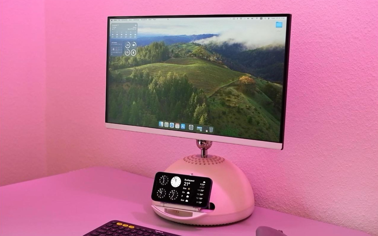 A computer monitor which was formerly an iMac G4 with a hemispherical white base sits on a table. The table and wall are likely white, but pink light is washing the scene making them and the monitor base appear pink. An iPhone sits above a piece of rounded plastic jutting out from the monitor base.