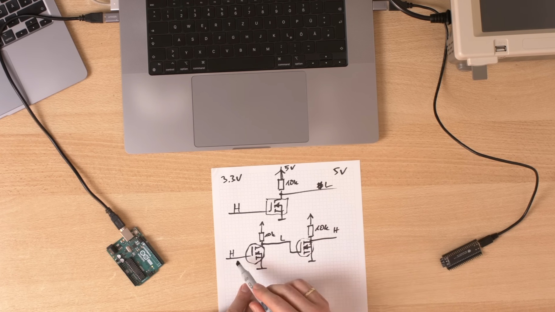 A circuit diagram in a book on a desk with computers and microcontrollers