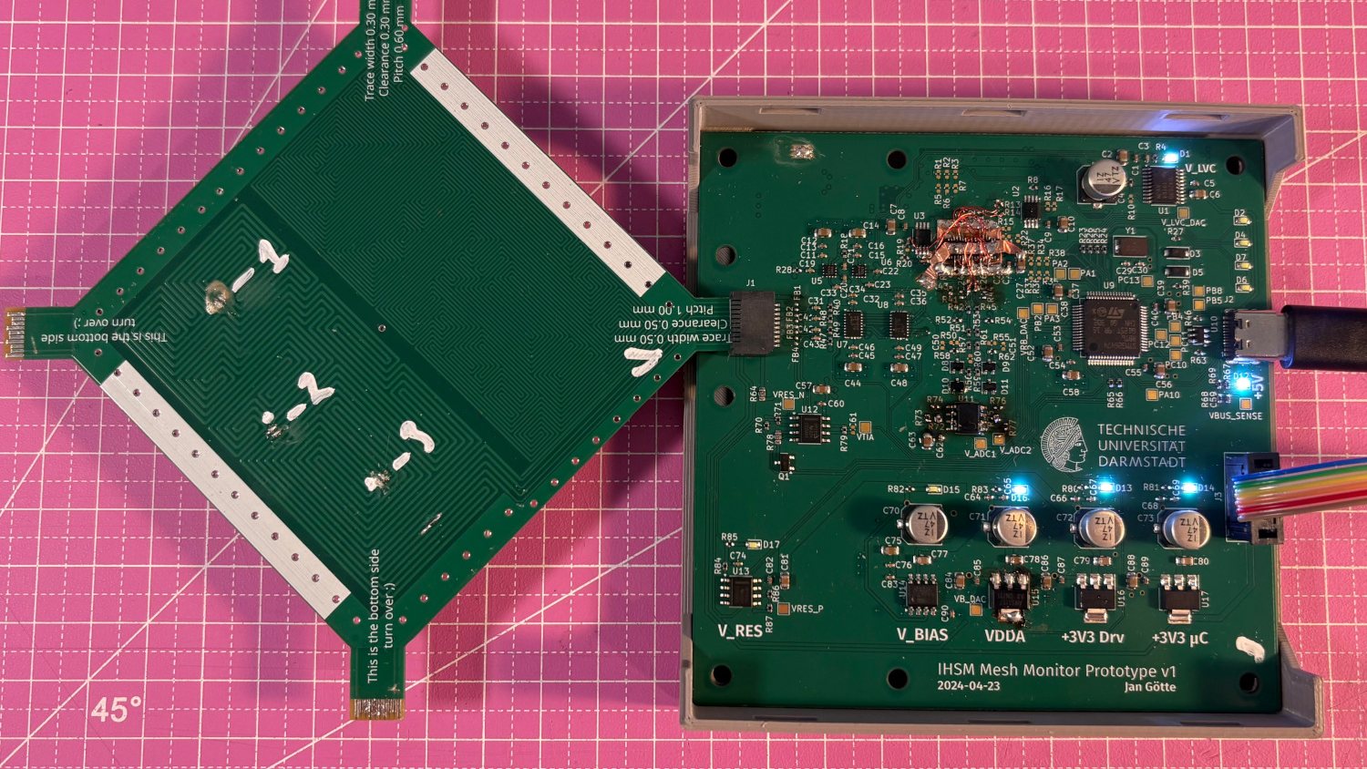 A pair of printed circuit boards are shown against a pink background. The right circuit board is plugged into a USB cable, and has several LED indicators on. The left board is plugged into the other at 45-degree angle, and has no visible components.