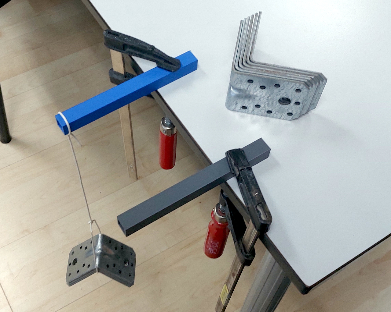 Two 150mm 3d printed box sections clamped to a table. One of them has a wire with some weights suspended from it.
