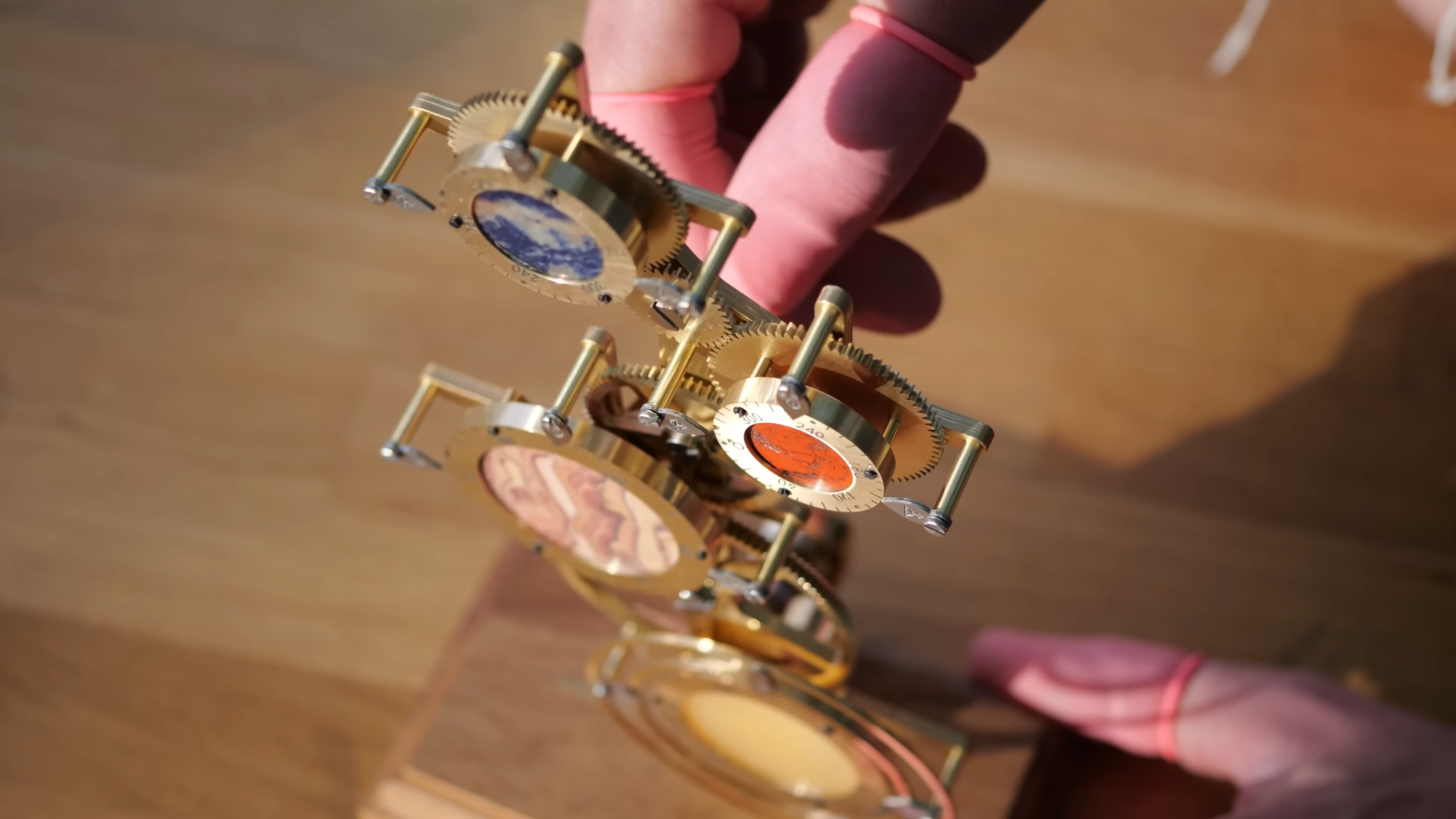 A brass and steel mechanism is shown, with a series of rotary dials on the front. Each dial is made out of a brass ring around the stone center. A man’s hand is behind the mechanism, turning a handle.