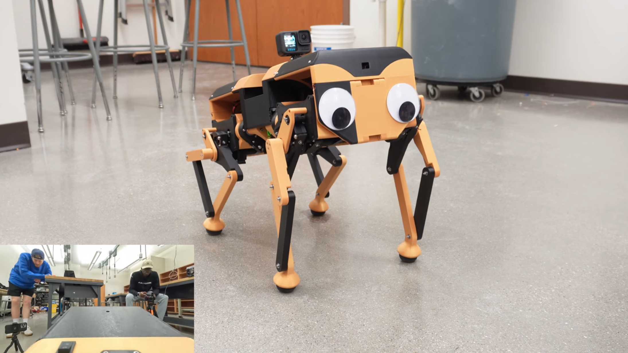 A black and yellow robot dog stands in the middle of the floor, with a GoPro camera mounted on its back. A picture-in-picture view in the bottom left corner shows the view from the camera.